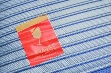 Red Fragile sticker on blue hard-cover suitcase surface to remind to handle with care