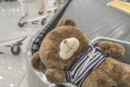 Cute brown teddy bear has been sadly abandoned alone on the moving baggage belt at the airportの写真素材