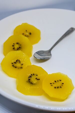 Slices of peeled juicy Golden kiwifruit on white plate and spoonの写真素材