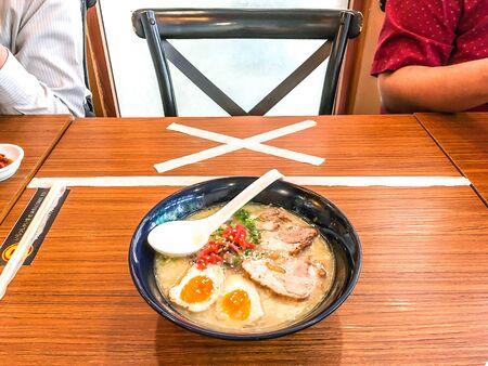 New normal of Social distancing policy in a Japanese Ramen restaurant, customers need to keep distance from each other. No sitting sign on dining table between two customers and the bowl of Ramenの写真素材
