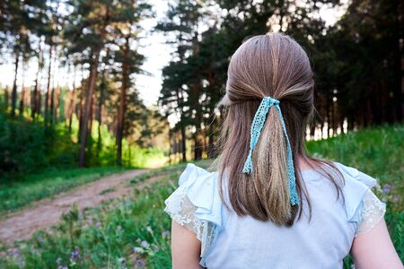 Head and shoulder back view of young blonde woman with blue lace braid in hairs. She looks at the...