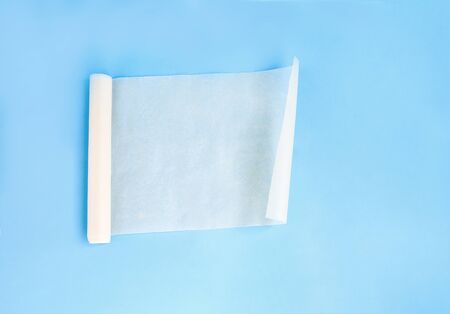 One new unfolded roll of clean baking paper brown color isolated on blue background. Crumpled piece of parchment. Top viewの写真素材