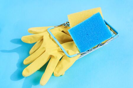 Blue and yellow sponges and gloves in metal basket on a blue background. Space for text. top viewの写真素材
