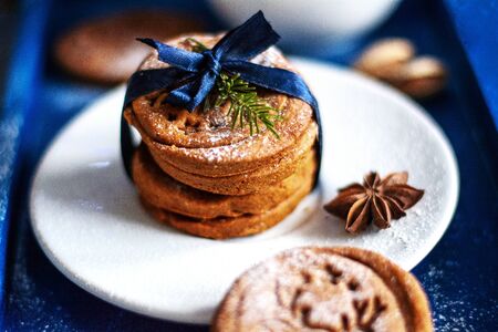 Creative Christmas homemade biscuits with blue ribbon and twig of fir on a white plate on blue...