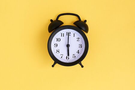 View from above on black alarm clock on blue background. 6 a.m.