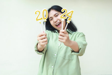 happy asian young woman hipster wearing green over size shirt screaming to camera with raising 2024 number candles holding on hand, isolated over white backgroundの写真素材