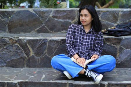 excited asian beautiful young woman college student smiling with happy face reading a book outdoor, campus university conceptの写真素材