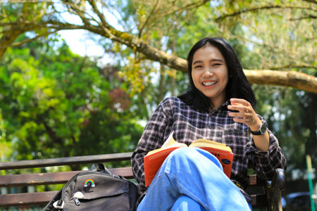 excited young asian woman college student laughing and smiling happy while read a book in the park, education conceptの写真素材