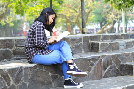happy mindful young asian woman college student reading a book in the park, education conceptの写真素材
