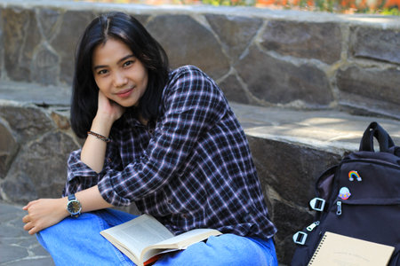 happy young asian woman college student with smiling face enjoy read a book for exam in the parkの写真素材