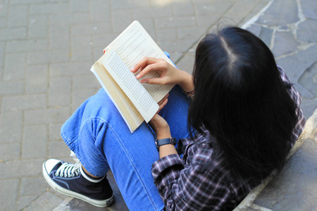 happy mindful young asian woman college student reading a book in the park, education concept