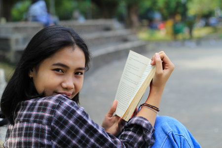 happy young asian woman college student with smiling face enjoy read a book for exam in the parkの写真素材
