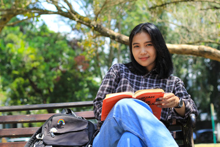 happy young asian woman college student with smiling face enjoy read a book for exam in the parkの写真素材