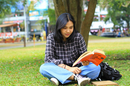happy and succes female asian college student enjoying read a book in the parkの写真素材