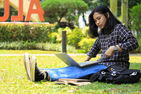portrait of focused young asian woman surfing internet using laptop to working remotely, read book, and writing in notebook. attractive asian student study in outdoorsの写真素材