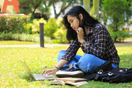 portrait of focused young asian woman surfing internet using laptop to working remotely, read book, and writing in notebook. attractive asian student study in outdoorsの写真素材