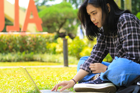 happy young asian woman focused using laptop  working remotely and browsing in social media in comfortable outdoors spaceの写真素材