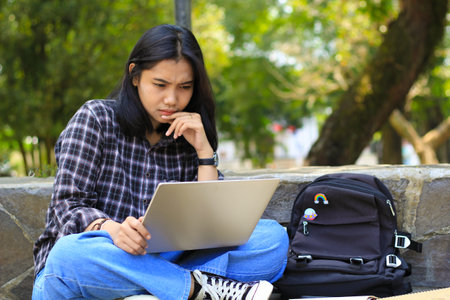 happy young asian woman focused using laptop  working remotely and browsing in social media in comfortable outdoors spaceの写真素材