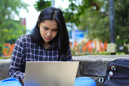 happy young asian woman focused using laptop  working remotely and browsing in social media in comfortable outdoors spaceの写真素材