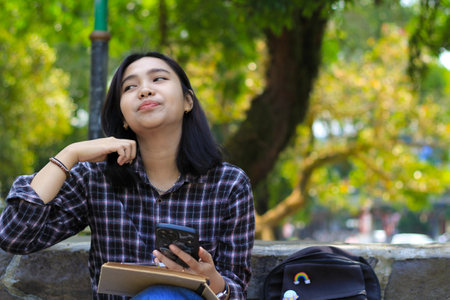 happy and joyful asian young bussines woman smiling hold mobile phone, writing in notebook or journal diary, student learningの写真素材