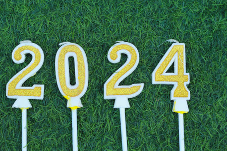 top view of glittering gold candle number 2024 above meadow with green grass, new year eve background conceptの写真素材
