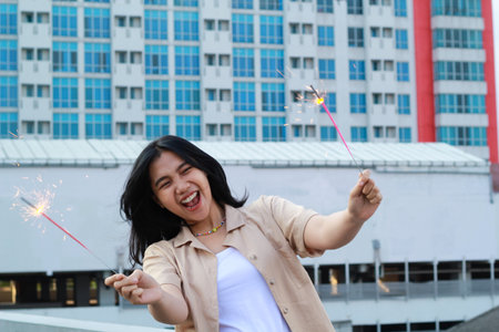 excited asian young woman holding sparkler to celebrating new year eve in rooftop apartment with city building backgroundの写真素材
