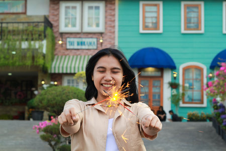 happy young asian woman holding sparkler celebrating new year eve in vintage house yard, outdoor gardenの写真素材