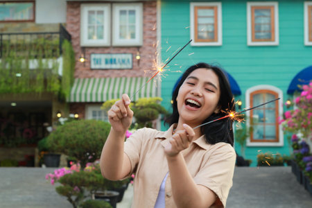 portrait of beautiful happy young asian woman holding sparklers fireworks to celebrate new year eve with garden party standing in outdoor vintage house yardの写真素材