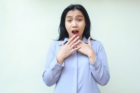shocked asian young woman wearing formal office clothes stunned looking at camera, covering her mouth wide open standing over isolated white backgroundの写真素材