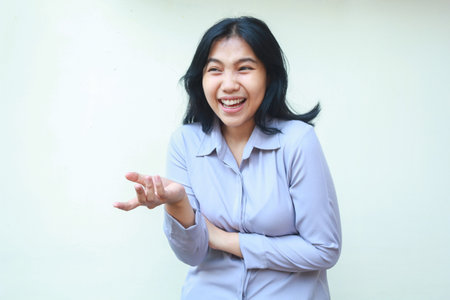 image of carefree asian business woman in formal office clothes laughing feeling pleased looking away raising open palm and folded arm presenting gesture standing over isolated white backgroundの写真素材