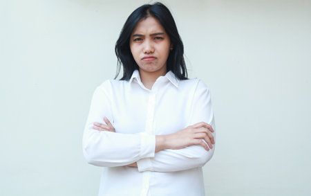 studio shot of sad gloomy asian woman boss frowning face angry look at camera with crossed arm wear white formal shirt standing over isolated backgroundの写真素材