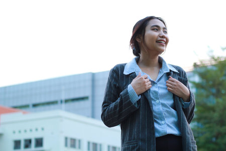 image of successful asian business woman walking in city streets with urban building background looking away confident wearing formal suit, female investment manager standing in outdoors smilingの写真素材
