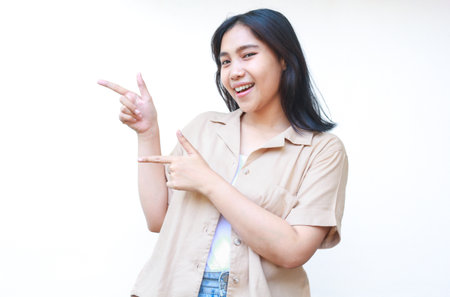 excited asian woman pointing finger showing presenting gesture wearing casual clothes isolated on white backgroundの写真素材
