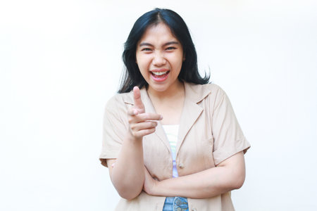happy asian woman laughing ecstatic and pointing finger to camera wearing casual brown clothes isolated on white backgroundの写真素材