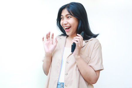 shocked asian woman holding smartphone looks amazed wearing casual clothes isolated on white backgroundの写真素材