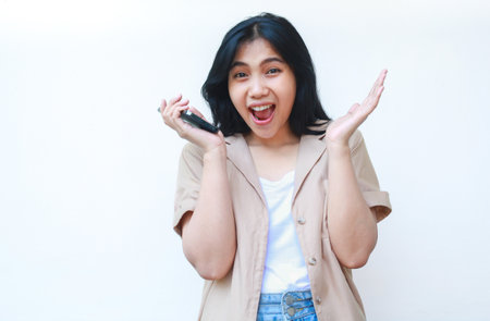 shocked asian woman holding smartphone looks amazed wearing casual clothes isolated on white backgroundの写真素材