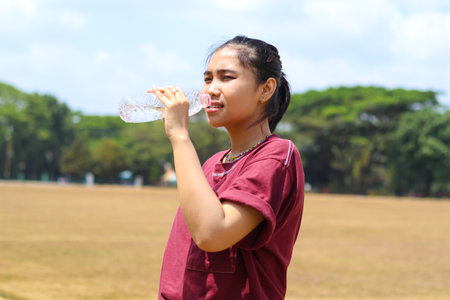 asian woman drink a bottle of water after running in outdoors in midday wearing casual t shirtの写真素材
