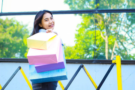 happy asian woman holding shopping bag smiling feels satisfied while walking in outdoors around mall buildingの写真素材