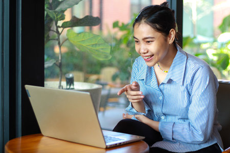 excited asian woman sitting in cafe talking on laptop have video chat, online meeting, with pointing...