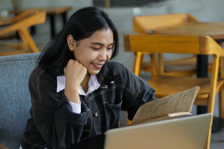 happy asian woman reading notebook and using laptop in library to studying