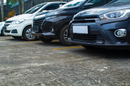 cars parked in a row in outdoor area of a mall car park have white, black, and grey color with palm...