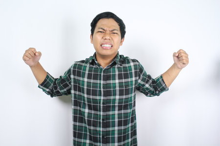 annoyed asian young man raising hand with unhappy expression while facing difficulty isolated white backgroundの写真素材