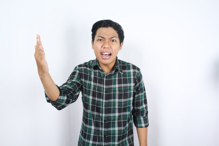 disappointed asian man raising hands with angry mad expression show questioning gesture isolatedの写真素材