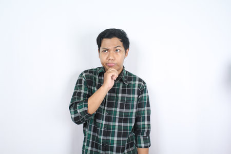 serious asian young man wearing casual clothes thinking about future with hand on chin isolated
