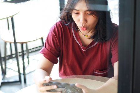 pretty asian woman surprised playing game online using smartphone sitting in outdoor cafe, high angle viewの写真素材