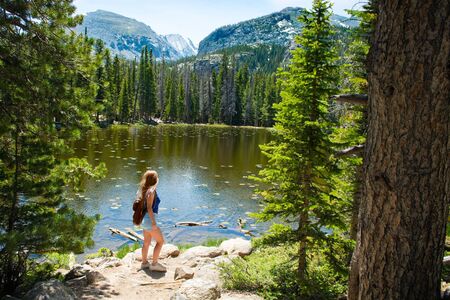 Girl relaxing on summer hiking trip. Woman enjoying beautiful view. Mountain landscape by the lake. Nymph Lake, Rocky Mountains National Park, Colorado, USA.の写真素材