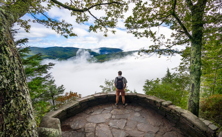 Man standing top of mountain, over clouds relaxing, enjoying beautiful foggy mountain landscape on his summer hiking trip. Near Asheville, Blue Ridge Mountains, North Carolina, USA.の写真素材