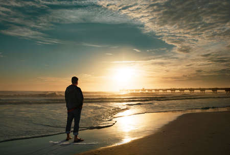 Man relaxing on the beautiful beach at sunrise. Sun rising over pier. Sun reflected on beach,...