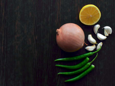 Onion, garlic, green chillies and lemon on wood table. Cooking ingredients concept. Healthy herbs on wood.の写真素材