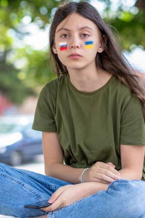 Close portrait of a child with Russian and Ukrainian flag colors. Outdoor portrait of a teenage girl with rebellious expression on her faceの写真素材